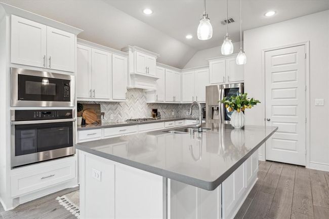 The spacious eat-in breakfast island is an ideal spot to start the morning and unwind in the evening, bringing everyone together for meaningful conversation and connection. Beautiful backsplash details and quartz countertops complete this sophisticated space. | Image 12