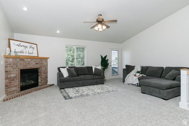 Carpeted living area with a ceiling fan, lofted ceiling, a fireplace, and recessed lighting | Image 4