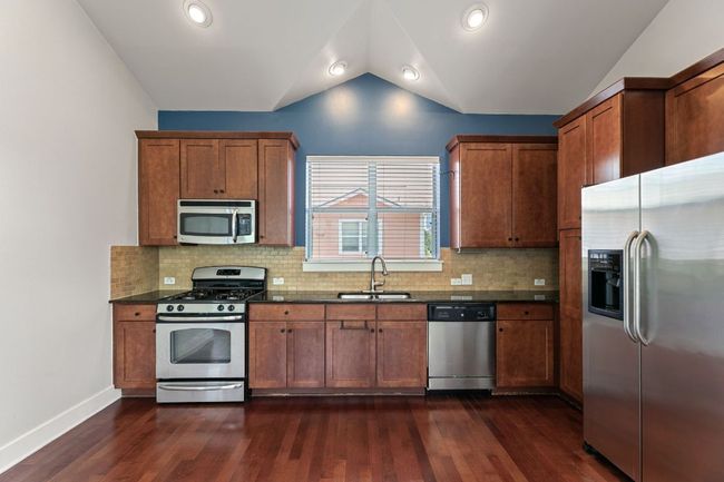 Kitchen with stainless steel appliances, vaulted ceiling, dark wood-style flooring, backsplash, and brown cabinetry | Image 4