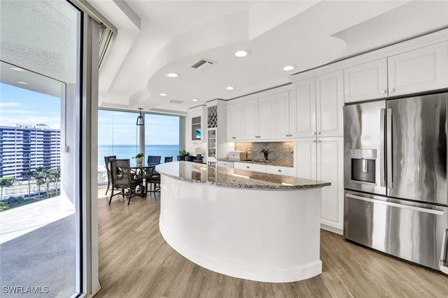 Kitchen with white cabinets, dark stone countertops, stainless steel fridge with ice dispenser, visible vents, and light wood-style floors | Image 13