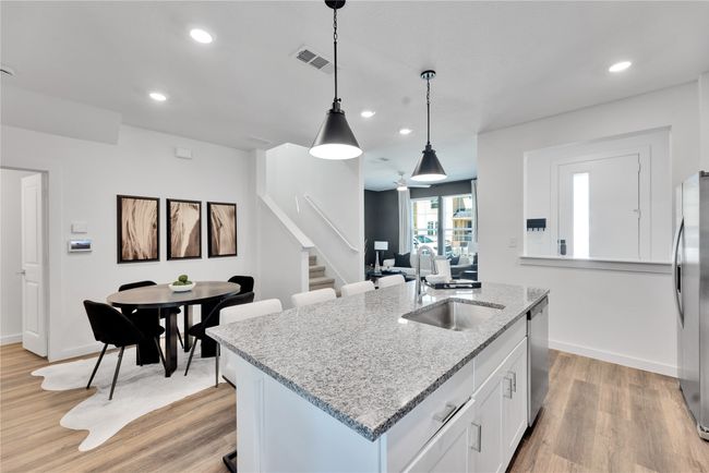 Kitchen featuring decorative light fixtures, light wood finished floors, visible vents, appliances with stainless steel finishes, and a sink | Image 10