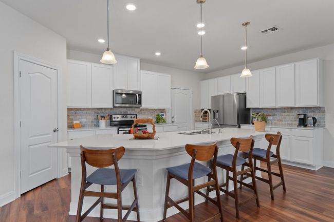 Kitchen featuring stainless steel appliances, backsplash, an island with sink, light countertops, and a kitchen breakfast bar | Image 9