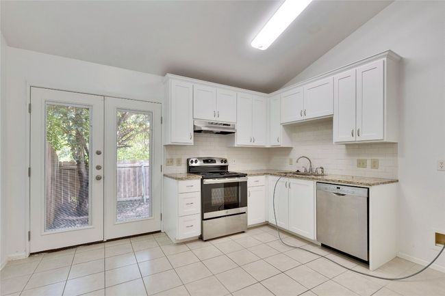 Kitchen featuring stainless steel appliances, backsplash, vaulted ceiling, french doors, and light stone countertops | Image 9
