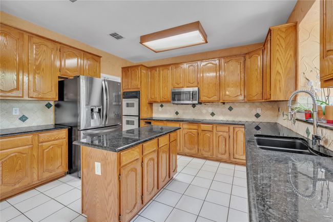 Kitchen featuring appliances with stainless steel finishes, dark stone counters, light tile patterned floors, and a center island | Image 6