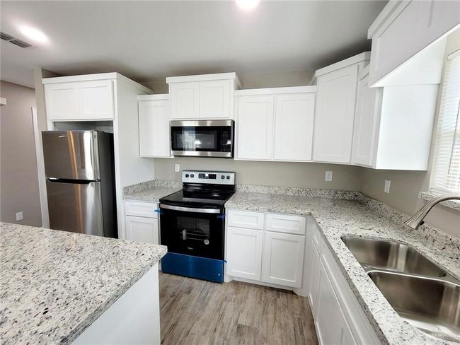 Kitchen featuring appliances with stainless steel finishes, white cabinets, light wood-style floors, and light stone countertops | Image 5