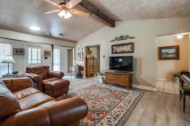 Living area with a textured wall, a ceiling fan, vaulted ceiling with beams, visible vents, and hardwood / wood-style flooring | Image 8