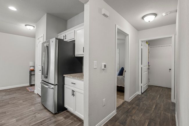 Kitchen with stainless steel fridge with ice dispenser, dark wood-style flooring, white cabinets, and light stone countertops | Image 18