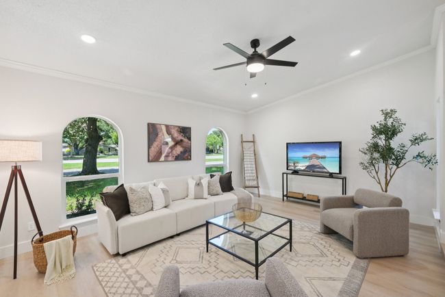 Living room with healthy amount of natural light, light wood-style flooring, ceiling fan, recessed lighting, and crown molding | Image 9