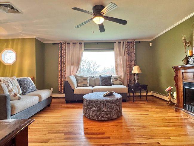 Living area with ornamental molding, visible vents, light wood finished floors, and a glass covered fireplace | Image 4