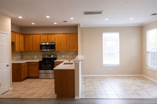 Kitchen featuring appliances with stainless steel finishes, a sink, brown cabinets, tasteful backsplash, and crown molding | Image 6