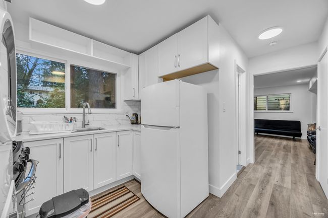 Kitchen with freestanding refrigerator, light countertops, white cabinets, light wood-style flooring, and backsplash | Image 26