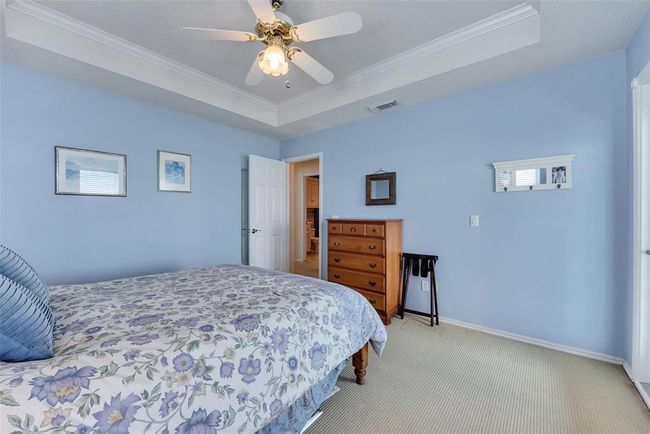 Soft blue walls and neutral flooring create a calming atmosphere in this secondary bedroom. The tray ceiling adds architectural interest while the layout offers ample space and flow to the adjoining bath. | Image 21