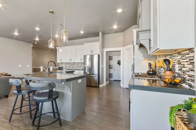 Kitchen featuring a sink, a kitchen island with sink, a kitchen bar, tasteful backsplash, and stainless steel refrigerator with ice dispenser | Image 6
