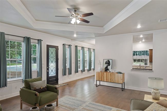 Living room featuring wood finished floors, crown molding, a ceiling fan, and a tray ceiling | Image 6