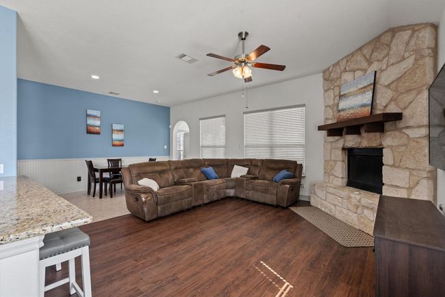 Living area featuring ceiling fan, a wainscoted wall, dark wood finished floors, a stone fireplace, and arched walkways | Image 9
