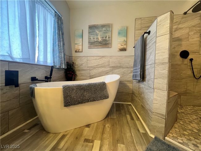 Full bathroom with tile walls, hardwood / wood-style floors, walk in shower, a soaking tub, and wainscoting | Image 44