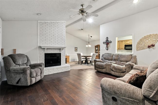 Living area with hardwood / wood-style flooring, a ceiling fan, vaulted ceiling, a textured ceiling, and a fireplace | Image 11