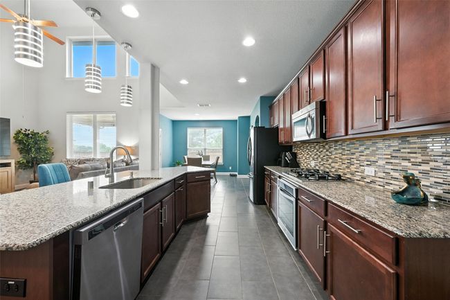 Kitchen with appliances with stainless steel finishes, a center island with sink, dark tile patterned floors, backsplash, and light stone counters | Image 13