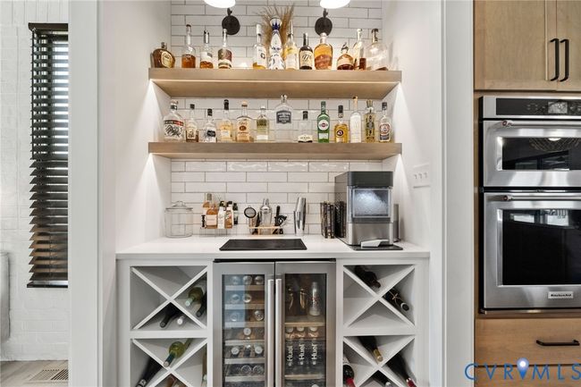 Indoor dry bar with tasteful backsplash, stainless steel double oven, and wine cooler | Image 13