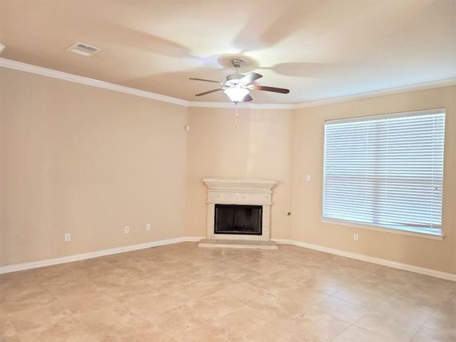 Unfurnished living room with ceiling fan, crown molding, a glass covered fireplace, baseboards, and light tile patterned floors | Image 14