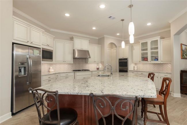 This modern kitchen features a spacious granite island with seating, stainless steel appliances, and elegant white cabinetry. The open layout, pendant lighting, and ample counter space make it ideal for cooking and entertaining. | Image 13