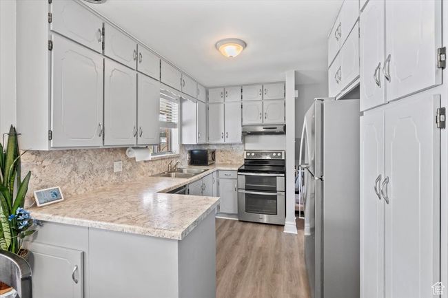 Kitchen featuring stainless steel appliances, under cabinet range hood, a sink, a peninsula, and light wood-type flooring | Image 9