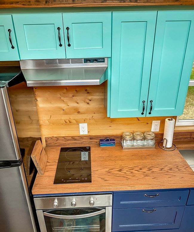 Kitchen with stainless steel oven, blue cabinets, under cabinet range hood, and black electric stovetop | Image 24