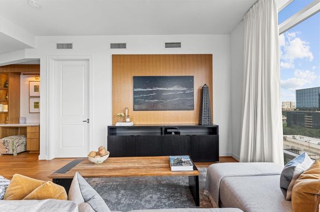 This modern living space features a cozy seating area with neutral tones, a sleek black console with decorative art, and large windows offering plenty of natural light and city views. Perfect for relaxation and entertaining. | Image 9