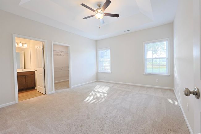Unfurnished bedroom with light carpet, a tray ceiling, connected bathroom, and a ceiling fan | Image 12