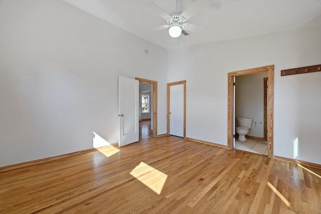 Unfurnished bedroom featuring light wood-type flooring, a ceiling fan, ensuite bath, baseboards, and a towering ceiling | Image 16