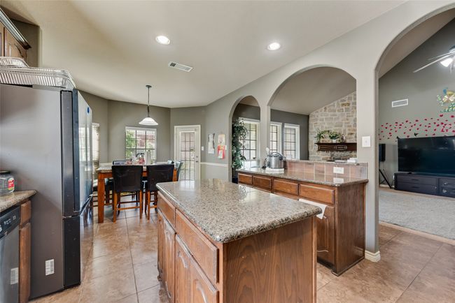 Kitchen with stainless steel appliances, a kitchen island, recessed lighting, light tile patterned floors, and light stone countertops | Image 9