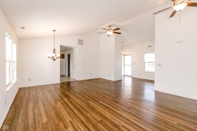 unfurnished living room featuring dark wood finished floors, vaulted ceiling, baseboards, visible vents, and ceiling fan with notable chandelier | Image 7