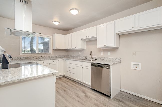 Kitchen featuring island exhaust hood, white cabinetry, stainless steel appliances, light wood-type flooring, and light stone counters | Image 14