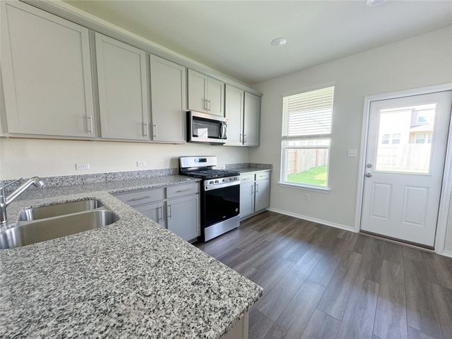Kitchen featuring stainless steel appliances, a sink, dark wood-type flooring, and light stone countertops | Image 4