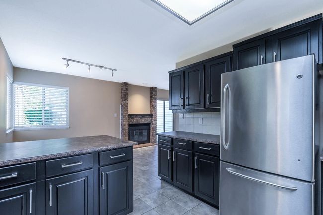 Kitchen featuring light tile patterned floors, backsplash, dark countertops, freestanding refrigerator, and a brick fireplace | Image 16