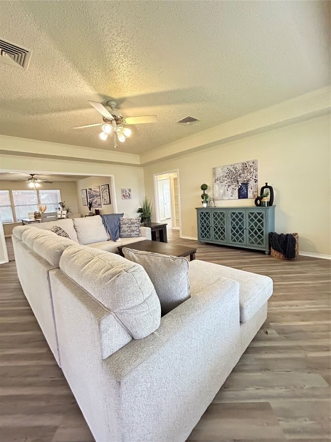 Living area with visible vents, a textured ceiling, ceiling fan, and wood finished floors | Image 6