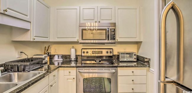 Kitchen featuring stainless steel appliances, dark countertops, and white cabinets | Image 11