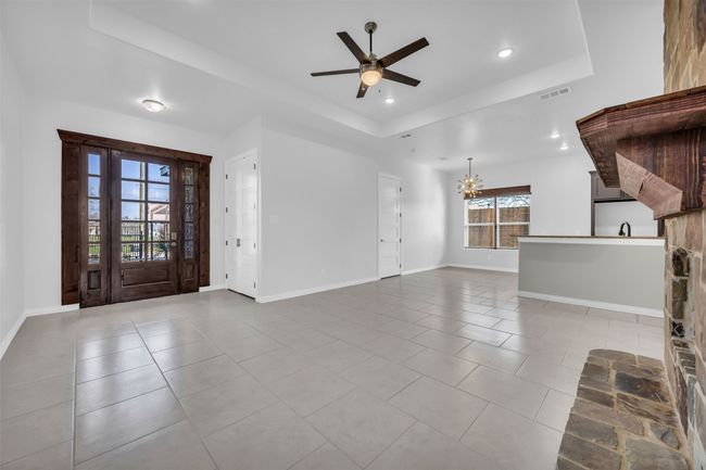 Unfurnished living room with a raised ceiling, ceiling fan with notable chandelier, and light tile patterned floors | Image 11