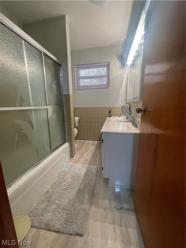 Full bathroom featuring wood-type flooring, shower / bath combination with glass door, oversized vanity, and toilet | Image 24