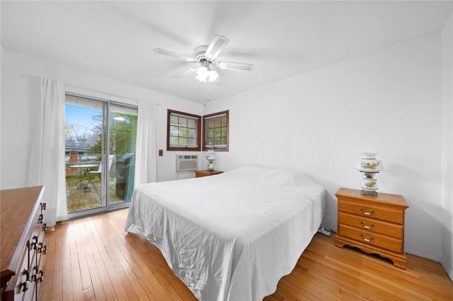 Bedroom featuring light wood finished floors, a wall mounted AC, ceiling fan, and access to exterior | Image 8
