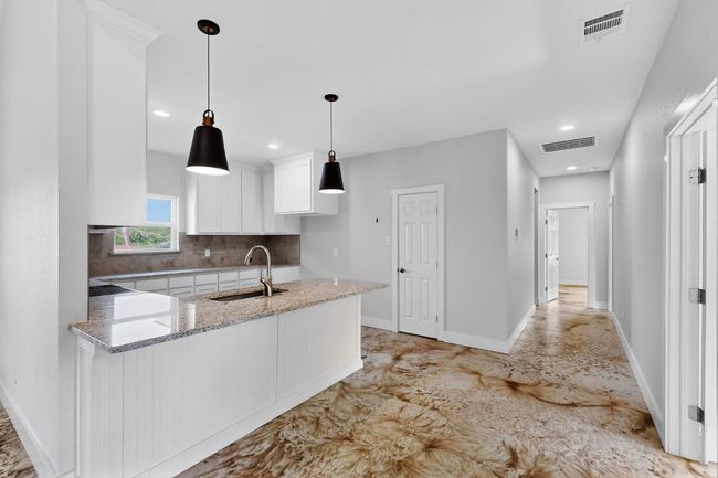 Kitchen with white cabinetry, a peninsula, light stone countertops, backsplash, and pendant lighting | Image 19