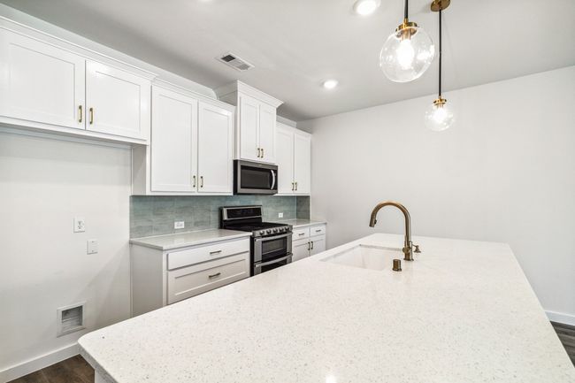 Kitchen with appliances with stainless steel finishes, a sink, a center island with sink, white cabinets, and decorative backsplash | Image 13