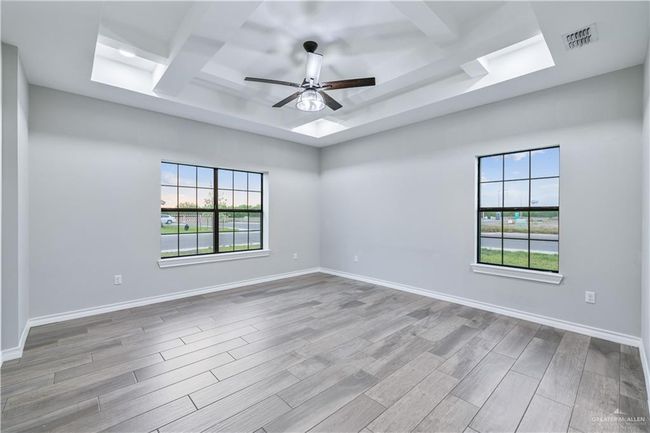 Spare room featuring a raised ceiling, a ceiling fan, plenty of natural light, and wood finished floors | Image 5