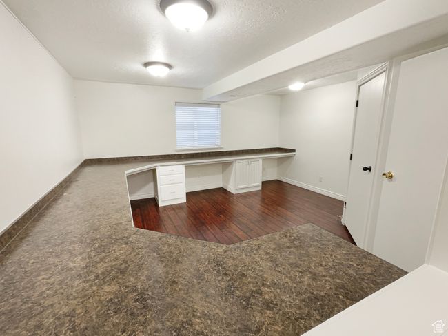 Unfurnished office with dark wood finished floors, built in study area, a textured ceiling, and baseboards | Image 25