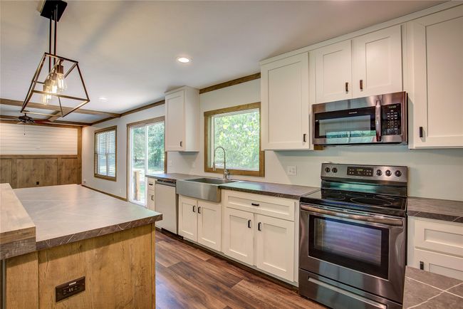 Kitchen featuring stainless steel appliances, dark countertops, white cabinets, wood walls, and dark wood-style flooring | Image 16