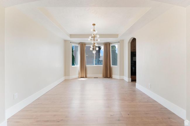 Formal dining area with arched walkways, a raised ceiling, a chandelier, and light wood-type flooring | Image 7