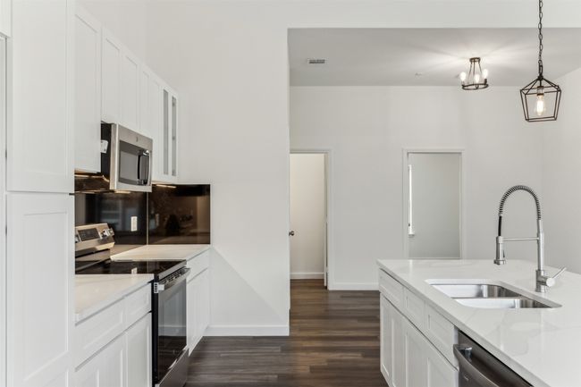 Kitchen with stainless steel appliances, dark wood-style flooring, white cabinetry, hanging light fixtures, and tasteful backsplash | Image 19