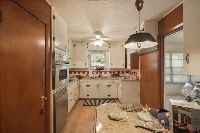 Kitchen open to family room but has access to front living room. Retro novelty shaped seating height island, newer appliances with stainless steel finishes, vintage ceramic decorative tile backsplash and white cabinets | Image 5