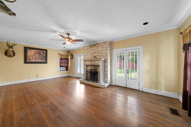 Unfurnished living room featuring ornamental molding, hardwood / wood-style flooring, a stone fireplace, french doors, and ceiling fan | Image 4