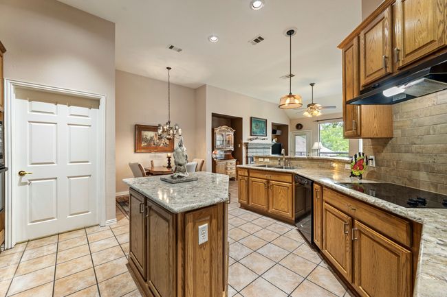 Kitchen with black appliances, a sink, under cabinet range hood, brown cabinets, and decorative backsplash | Image 17